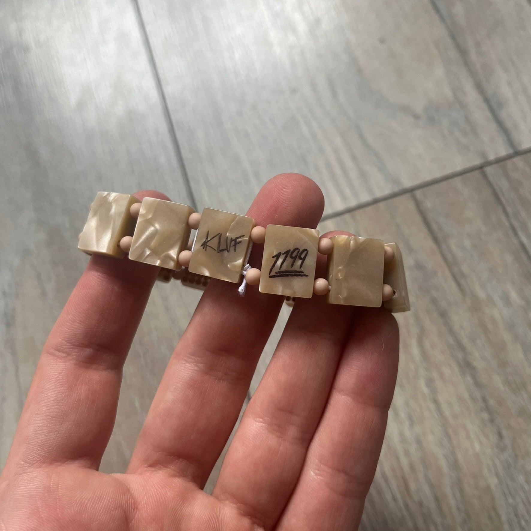 Bazo 1199 x 63KLUF Rhinestone Bracelet is a wooden bead bracelet from the 1199 and 63KLUF collaboration. The outer side is covered with gold and orange-toned rhinestones, while the inner side has a pearly beige finish. The interior is marked with black 1199 and 63KLUF logos.
