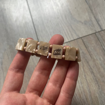 Bazo 1199 x 63KLUF Rhinestone Bracelet is a wooden bead bracelet from the 1199 and 63KLUF collaboration. The outer side is covered with gold and orange-toned rhinestones, while the inner side has a pearly beige finish. The interior is marked with black 1199 and 63KLUF logos.