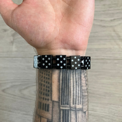 Bazo 1199 “Black on White” Stars Bracelet is a acetate bead bracelet featuring black beads with white star graphics printed on the tops and sides. One bead is marked with a red 1199 logo on the inside. It comes with the original foil packaging.
