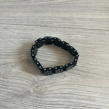 Bazo 1199 “Black on White” Stars Bracelet is a acetate bead bracelet featuring black beads with white star graphics printed on the tops and sides. One bead is marked with a red 1199 logo on the inside. It comes with the original foil packaging.
