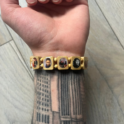 Beige “Forever 27 Club” bracelet by Bazo 1199, showcasing painted wooden beads and engraved portraits of legendary artists from the infamous 27 Club like Kurt Cobain, Basquiat, and Fredo Santana. Signed “forever 27 club” and “1199” on the inside.