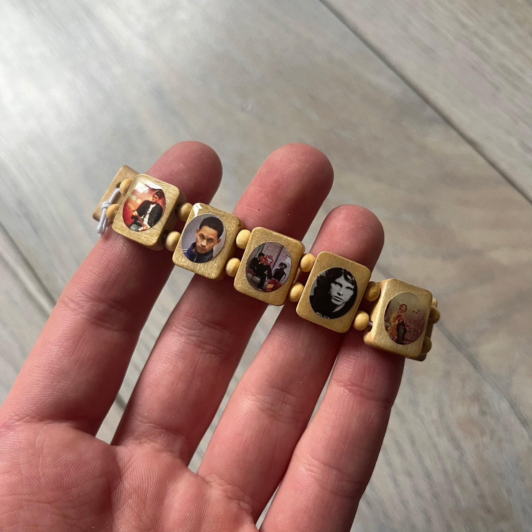 Beige “Forever 27 Club” bracelet by Bazo 1199, showcasing painted wooden beads and engraved portraits of legendary artists from the infamous 27 Club like Kurt Cobain, Basquiat, and Fredo Santana. Signed “forever 27 club” and “1199” on the inside.