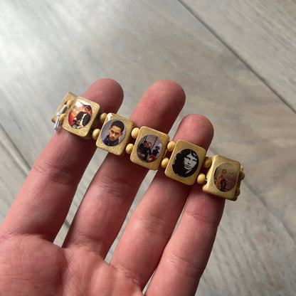 Beige “Forever 27 Club” bracelet by Bazo 1199, showcasing painted wooden beads and engraved portraits of legendary artists from the infamous 27 Club like Kurt Cobain, Basquiat, and Fredo Santana. Signed “forever 27 club” and “1199” on the inside.