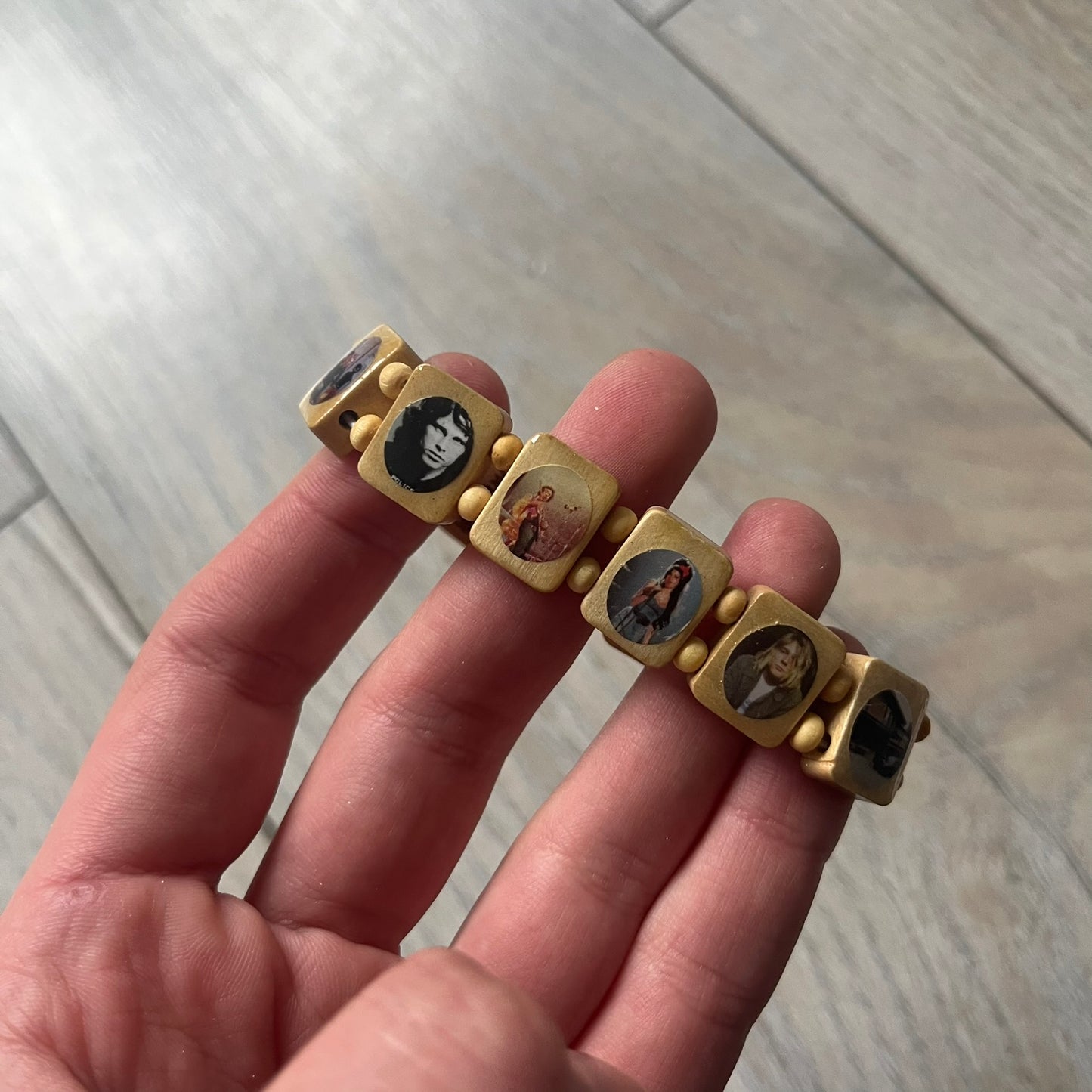 Beige “Forever 27 Club” bracelet by Bazo 1199, showcasing painted wooden beads and engraved portraits of legendary artists from the infamous 27 Club like Kurt Cobain, Basquiat, and Fredo Santana. Signed “forever 27 club” and “1199” on the inside.