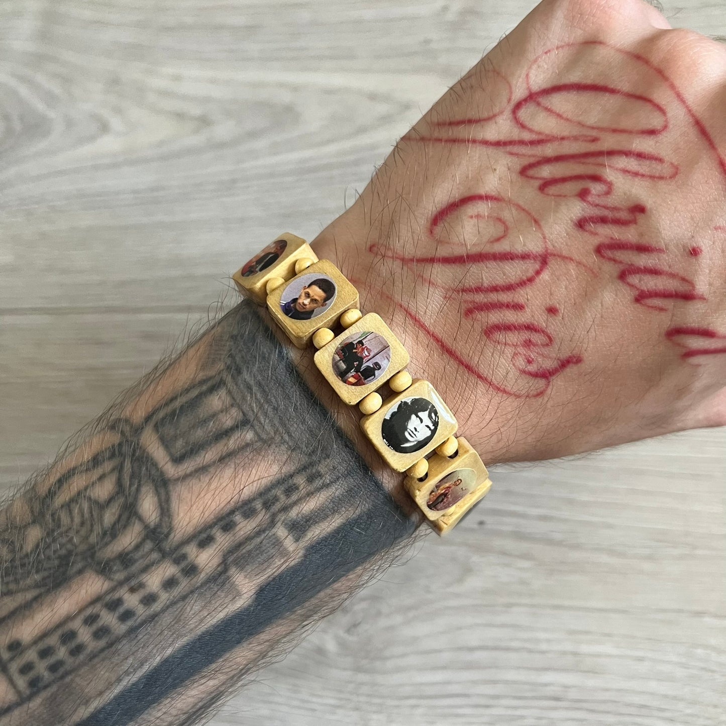 Beige “Forever 27 Club” bracelet by Bazo 1199, showcasing painted wooden beads and engraved portraits of legendary artists from the infamous 27 Club like Kurt Cobain, Basquiat, and Fredo Santana. Signed “forever 27 club” and “1199” on the inside.