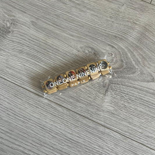 Beige “Forever 27 Club” bracelet by Bazo 1199, showcasing painted wooden beads and engraved portraits of legendary artists from the infamous 27 Club like Kurt Cobain, Basquiat, and Fredo Santana. Signed “forever 27 club” and “1199” on the inside.