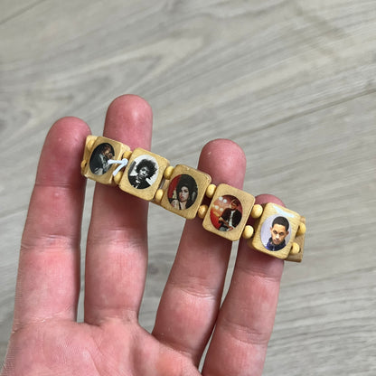 Beige “Forever 27 Club” bracelet by Bazo 1199, showcasing painted wooden beads and engraved portraits of legendary artists from the infamous 27 Club like Kurt Cobain, Basquiat, and Fredo Santana. Signed “forever 27 club” and “1199” on the inside.