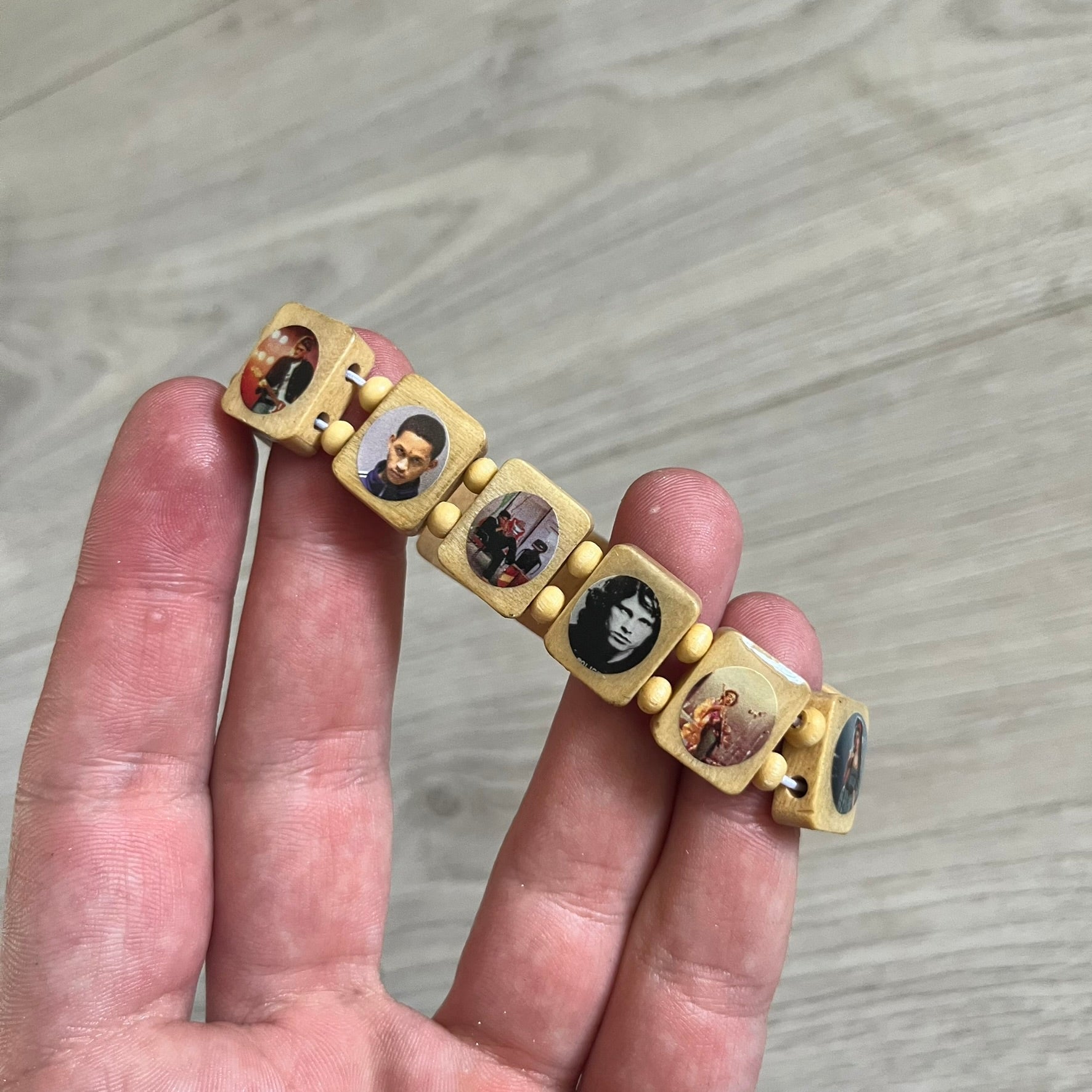 Beige “Forever 27 Club” bracelet by Bazo 1199, showcasing painted wooden beads and engraved portraits of legendary artists from the infamous 27 Club like Kurt Cobain, Basquiat, and Fredo Santana. Signed “forever 27 club” and “1199” on the inside.