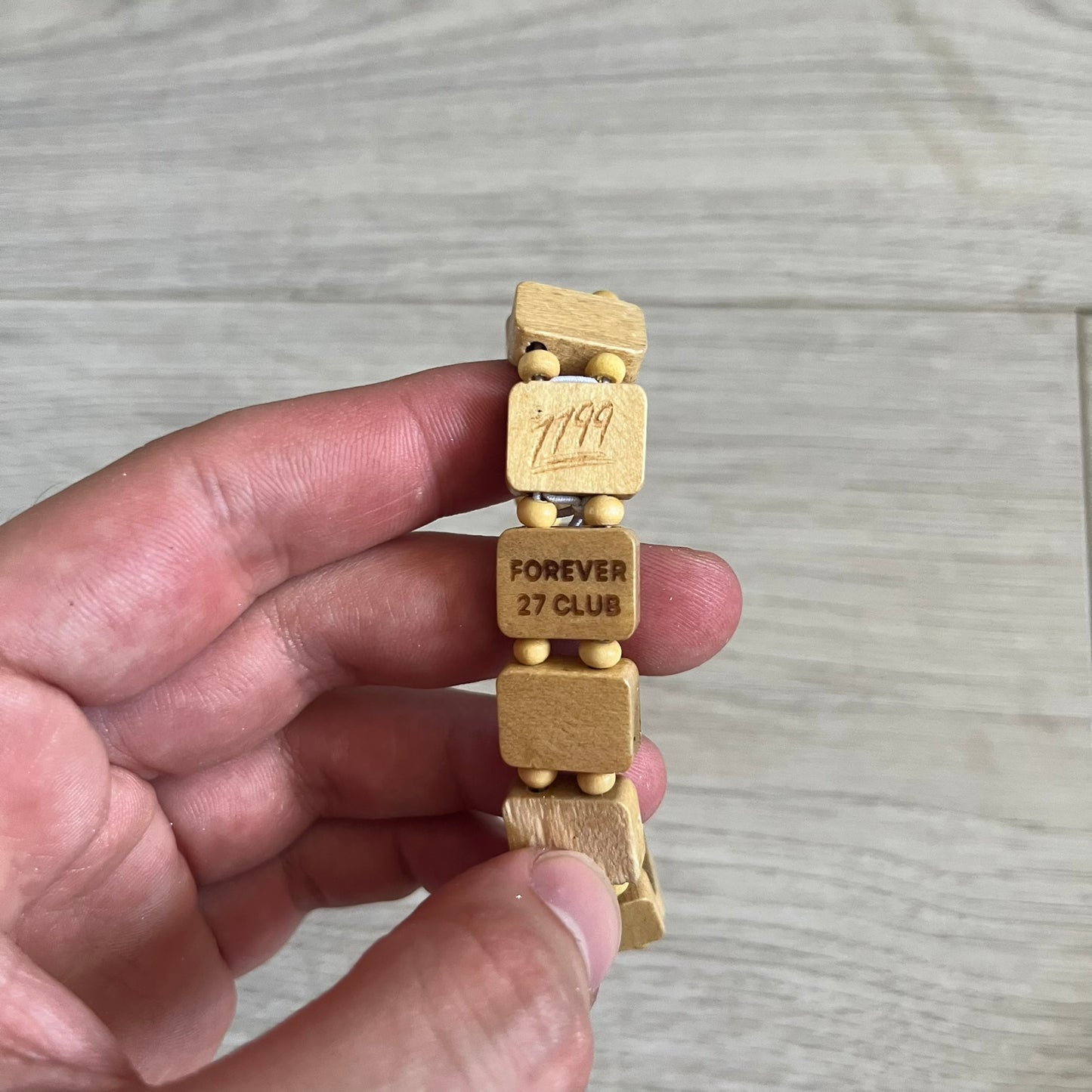 Beige “Forever 27 Club” bracelet by Bazo 1199, showcasing painted wooden beads and engraved portraits of legendary artists from the infamous 27 Club like Kurt Cobain, Basquiat, and Fredo Santana. Signed “forever 27 club” and “1199” on the inside.