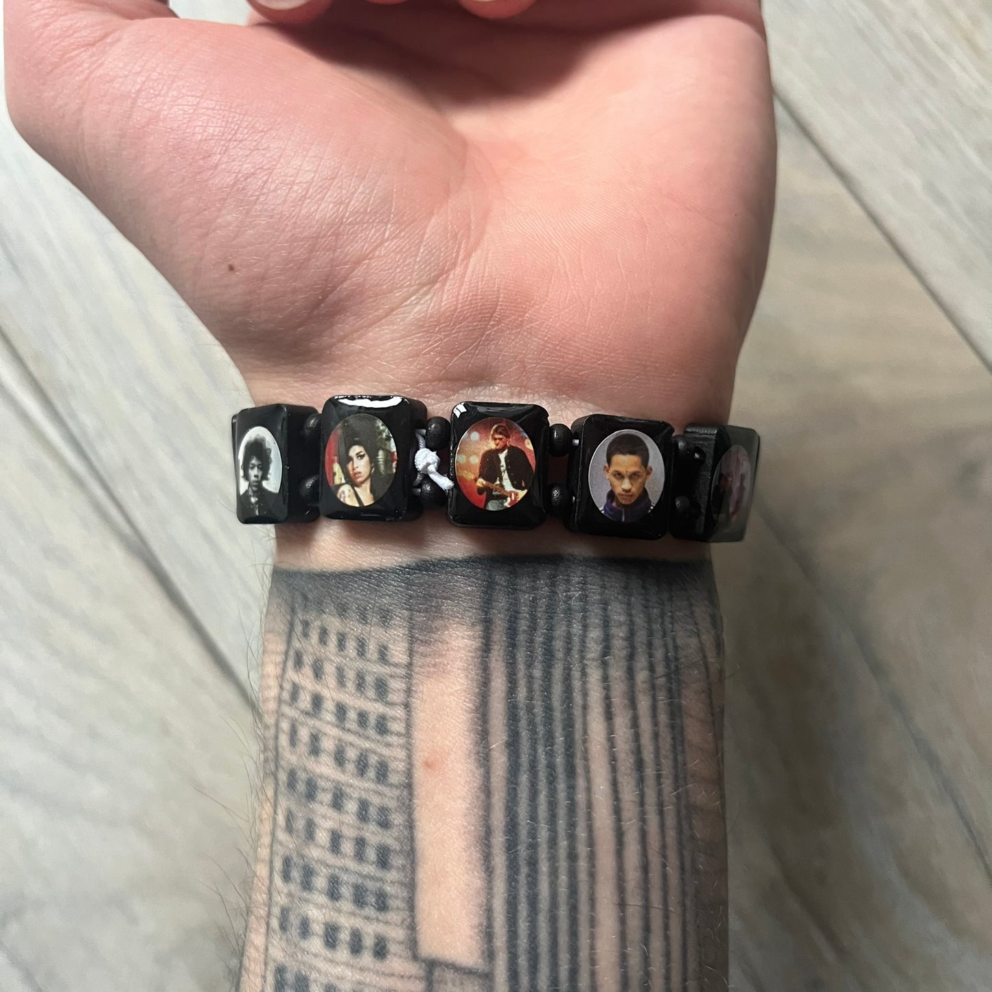 Black “Forever 27 Club” bracelet by Bazo 1199, showcasing painted wooden beads and engraved portraits of legendary artists from the infamous 27 Club like Kurt Cobain, Basquiat, and Fredo Santana. Signed “forever 27 club” and “1199” on the inside.