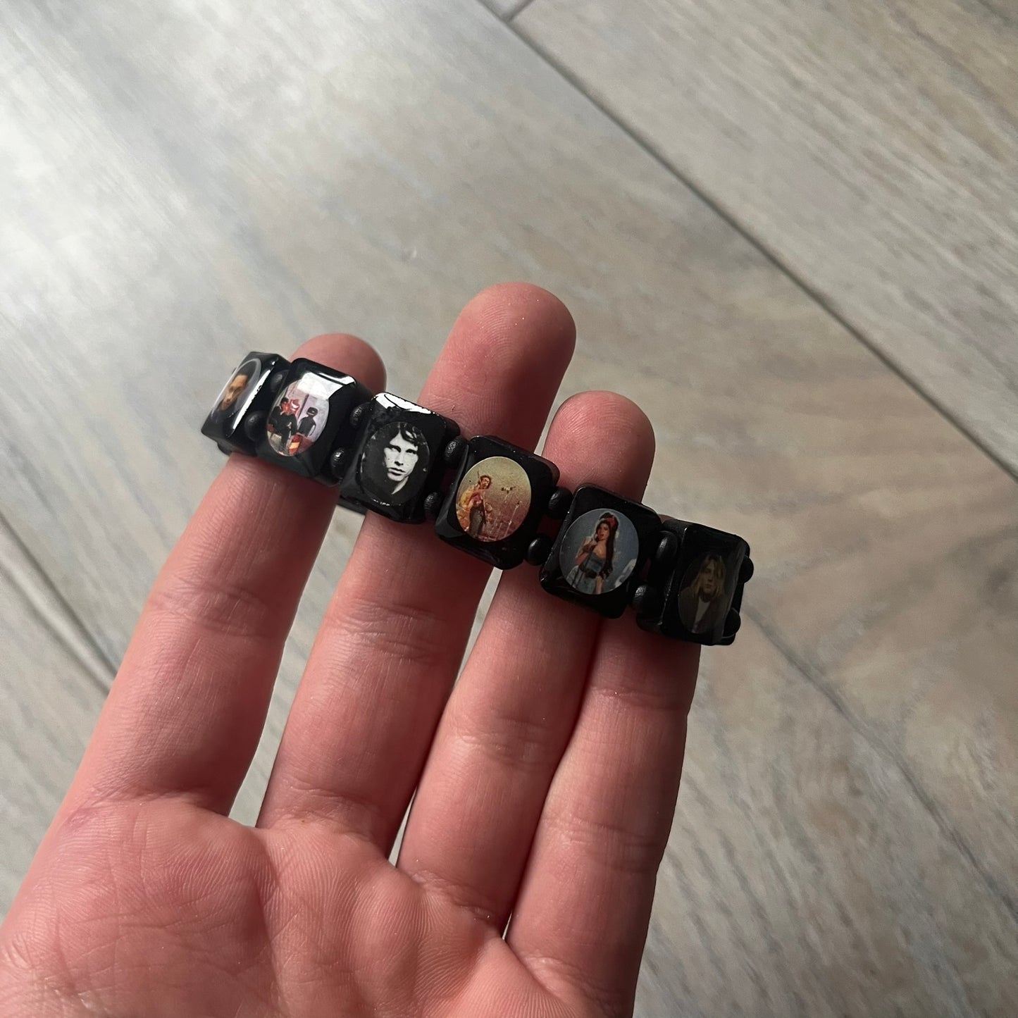 Black “Forever 27 Club” bracelet by Bazo 1199, showcasing painted wooden beads and engraved portraits of legendary artists from the infamous 27 Club like Kurt Cobain, Basquiat, and Fredo Santana. Signed “forever 27 club” and “1199” on the inside.