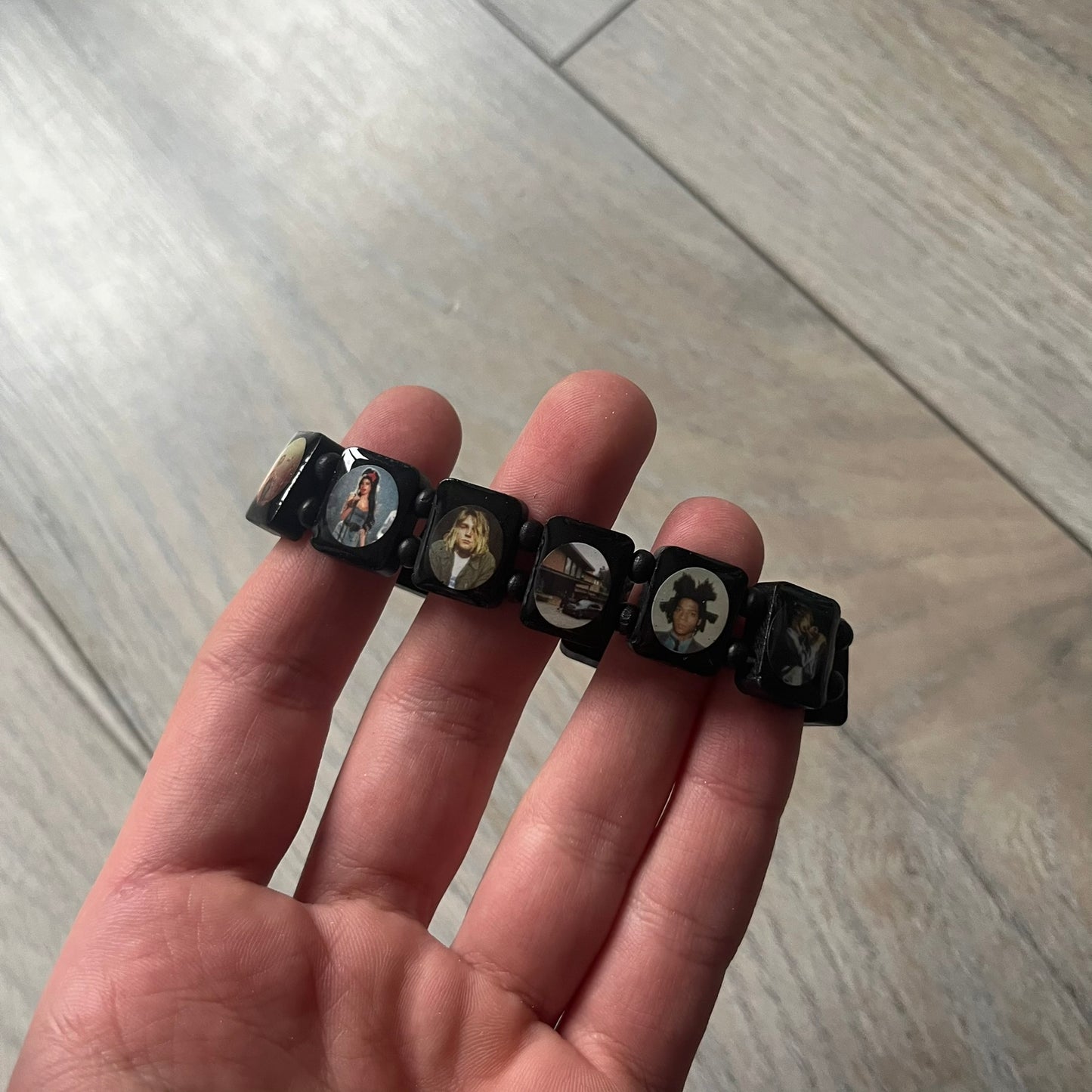 Black “Forever 27 Club” bracelet by Bazo 1199, showcasing painted wooden beads and engraved portraits of legendary artists from the infamous 27 Club like Kurt Cobain, Basquiat, and Fredo Santana. Signed “forever 27 club” and “1199” on the inside.