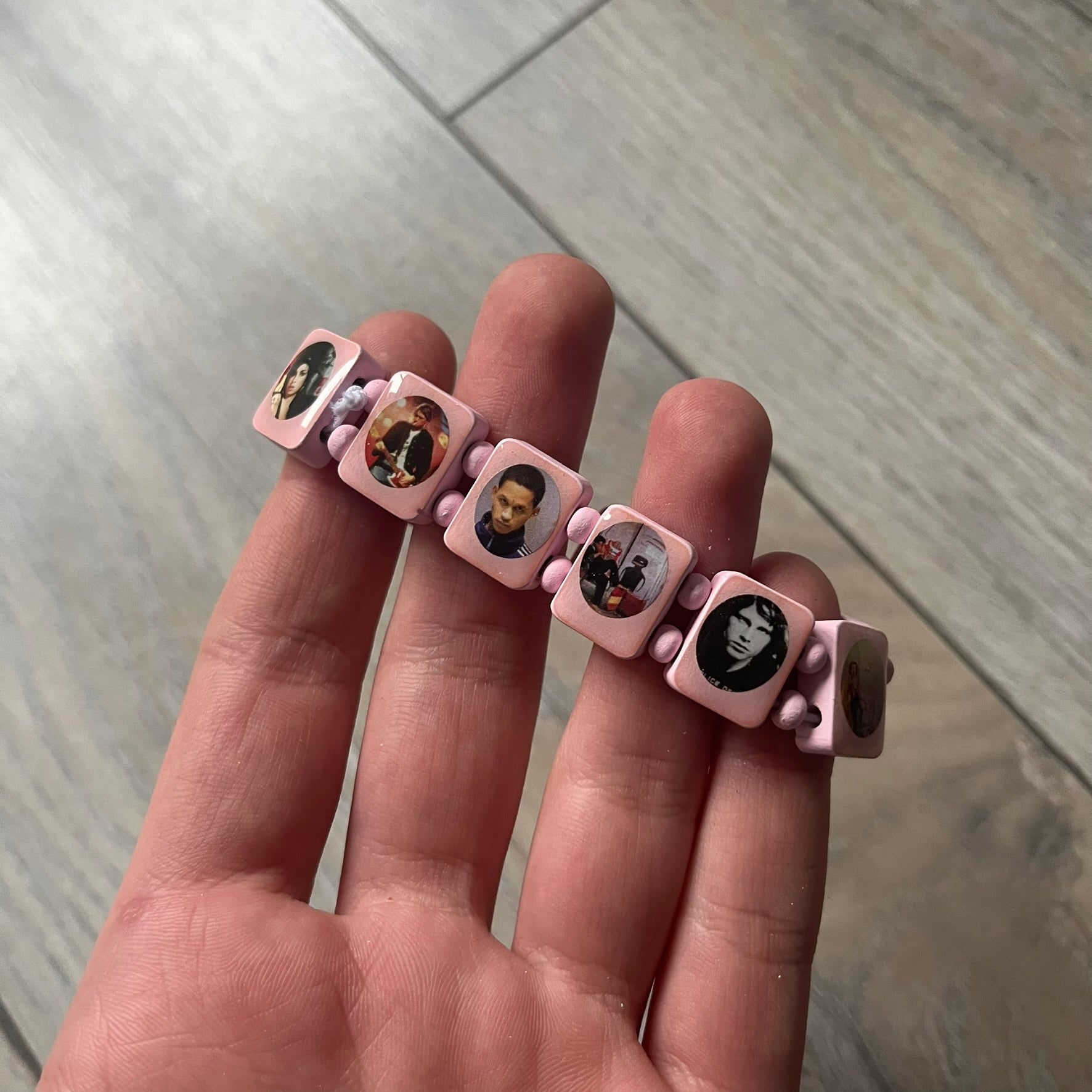 Blushing Bride “Forever 27 Club” bracelet by Bazo 1199, showcasing painted wooden beads and engraved portraits of legendary artists from the infamous 27 Club like Kurt Cobain, Basquiat, and Fredo Santana. Signed “forever 27 club” and “1199” on the inside.