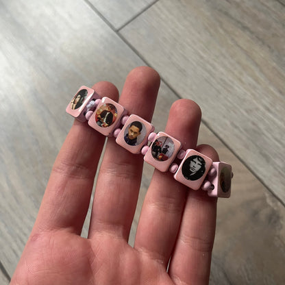 Blushing Bride “Forever 27 Club” bracelet by Bazo 1199, showcasing painted wooden beads and engraved portraits of legendary artists from the infamous 27 Club like Kurt Cobain, Basquiat, and Fredo Santana. Signed “forever 27 club” and “1199” on the inside.
