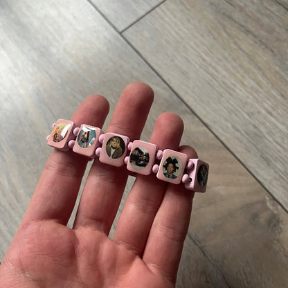 Blushing Bride “Forever 27 Club” bracelet by Bazo 1199, showcasing painted wooden beads and engraved portraits of legendary artists from the infamous 27 Club like Kurt Cobain, Basquiat, and Fredo Santana. Signed “forever 27 club” and “1199” on the inside.