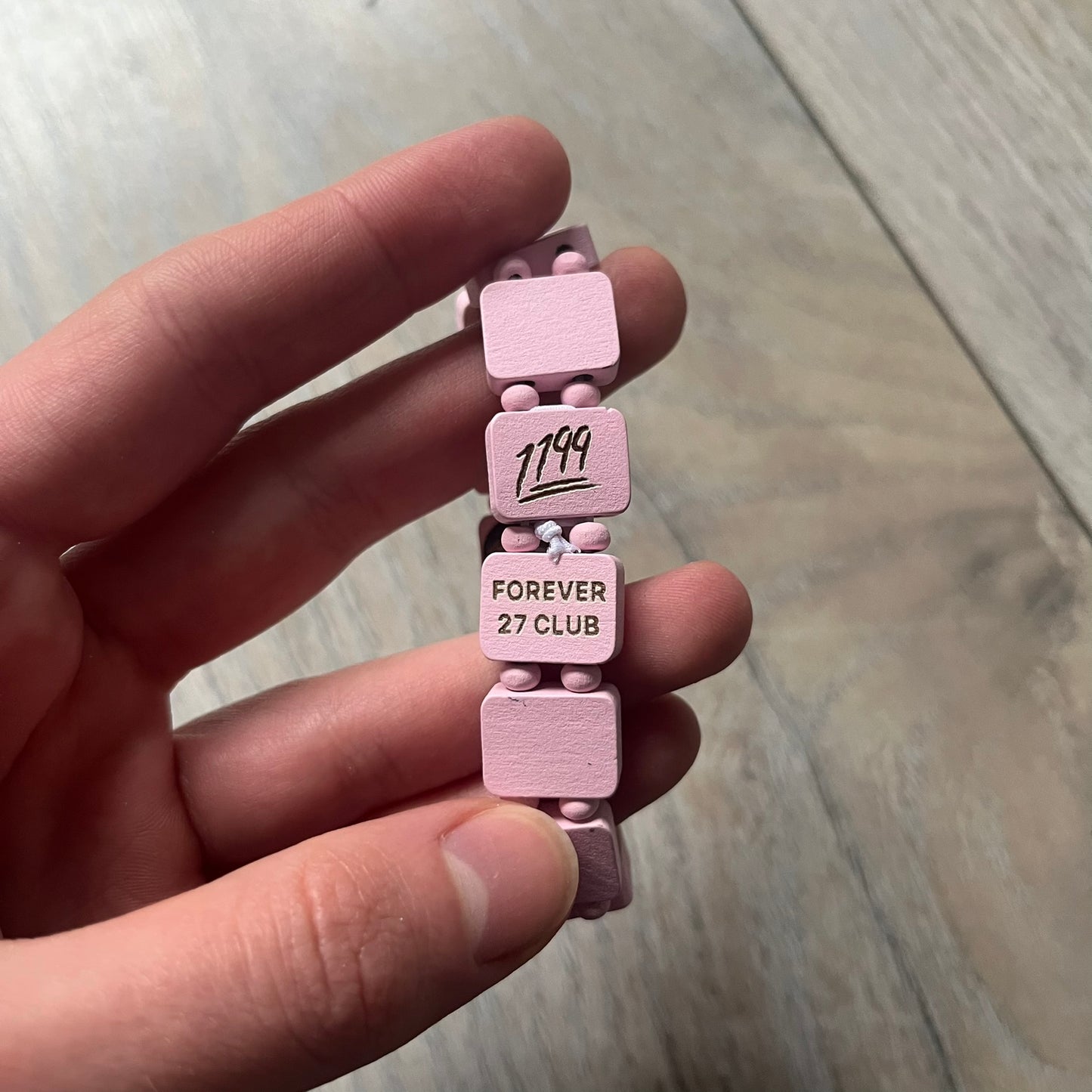 Blushing Bride “Forever 27 Club” bracelet by Bazo 1199, showcasing painted wooden beads and engraved portraits of legendary artists from the infamous 27 Club like Kurt Cobain, Basquiat, and Fredo Santana. Signed “forever 27 club” and “1199” on the inside.