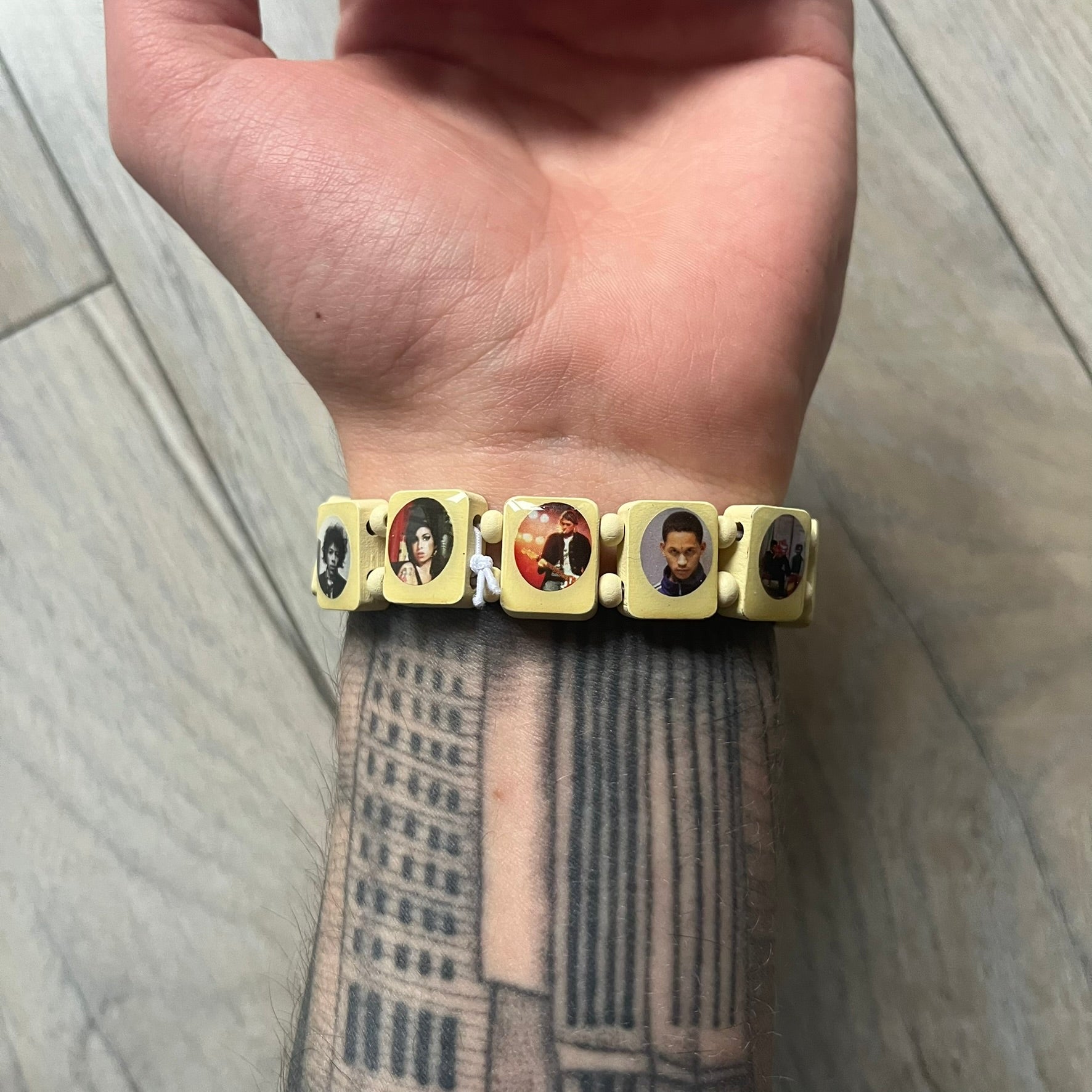 Pastel Yellow “Forever 27 Club” bracelet by Bazo 1199, showcasing painted wooden beads and engraved portraits of legendary artists from the infamous 27 Club like Kurt Cobain, Basquiat, and Fredo Santana. Signed “forever 27 club” and “1199” on the inside.