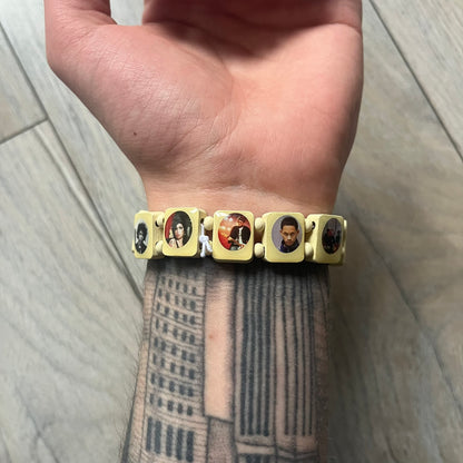 Pastel Yellow “Forever 27 Club” bracelet by Bazo 1199, showcasing painted wooden beads and engraved portraits of legendary artists from the infamous 27 Club like Kurt Cobain, Basquiat, and Fredo Santana. Signed “forever 27 club” and “1199” on the inside.
