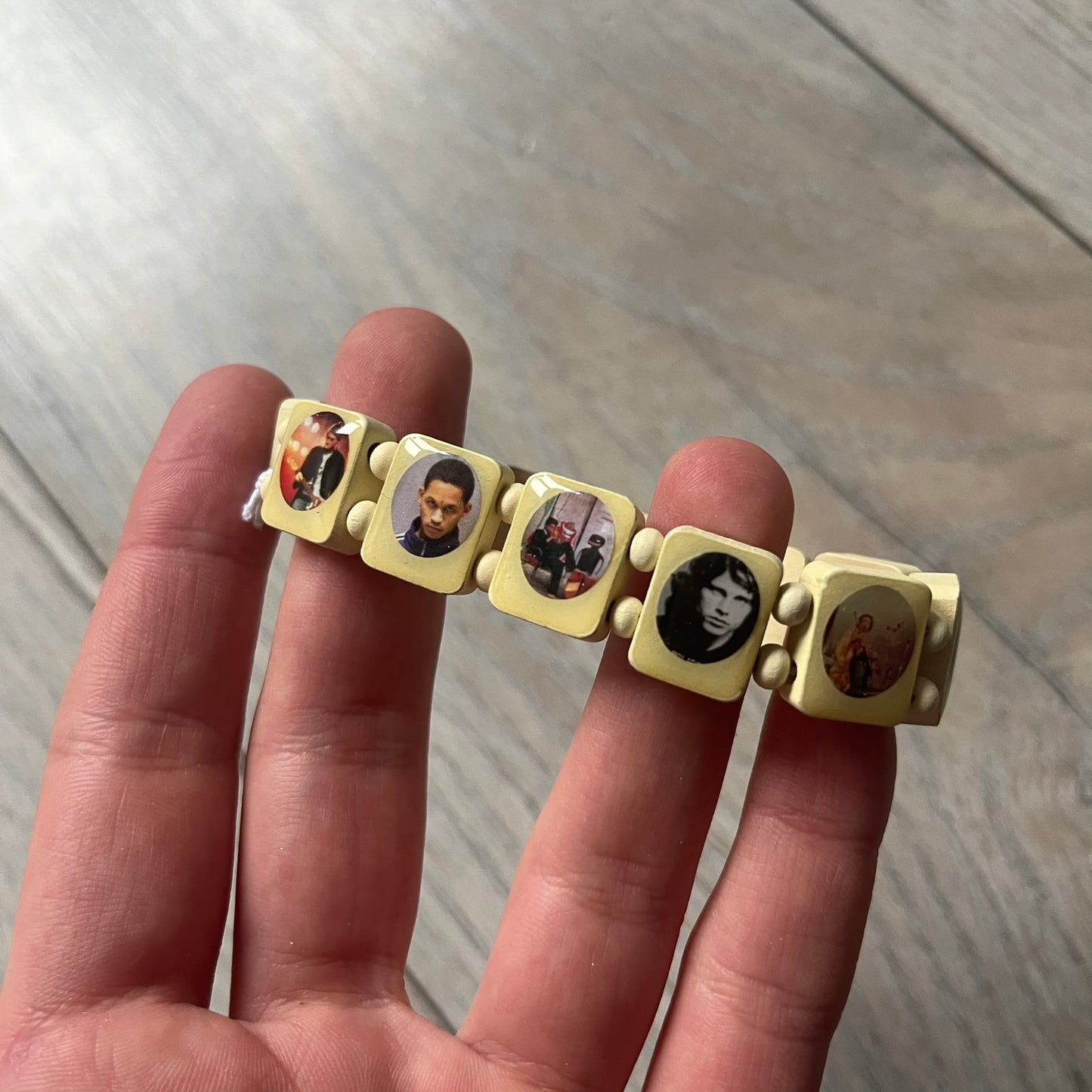 Pastel Yellow “Forever 27 Club” bracelet by Bazo 1199, showcasing painted wooden beads and engraved portraits of legendary artists from the infamous 27 Club like Kurt Cobain, Basquiat, and Fredo Santana. Signed “forever 27 club” and “1199” on the inside.
