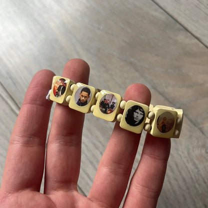 Pastel Yellow “Forever 27 Club” bracelet by Bazo 1199, showcasing painted wooden beads and engraved portraits of legendary artists from the infamous 27 Club like Kurt Cobain, Basquiat, and Fredo Santana. Signed “forever 27 club” and “1199” on the inside.