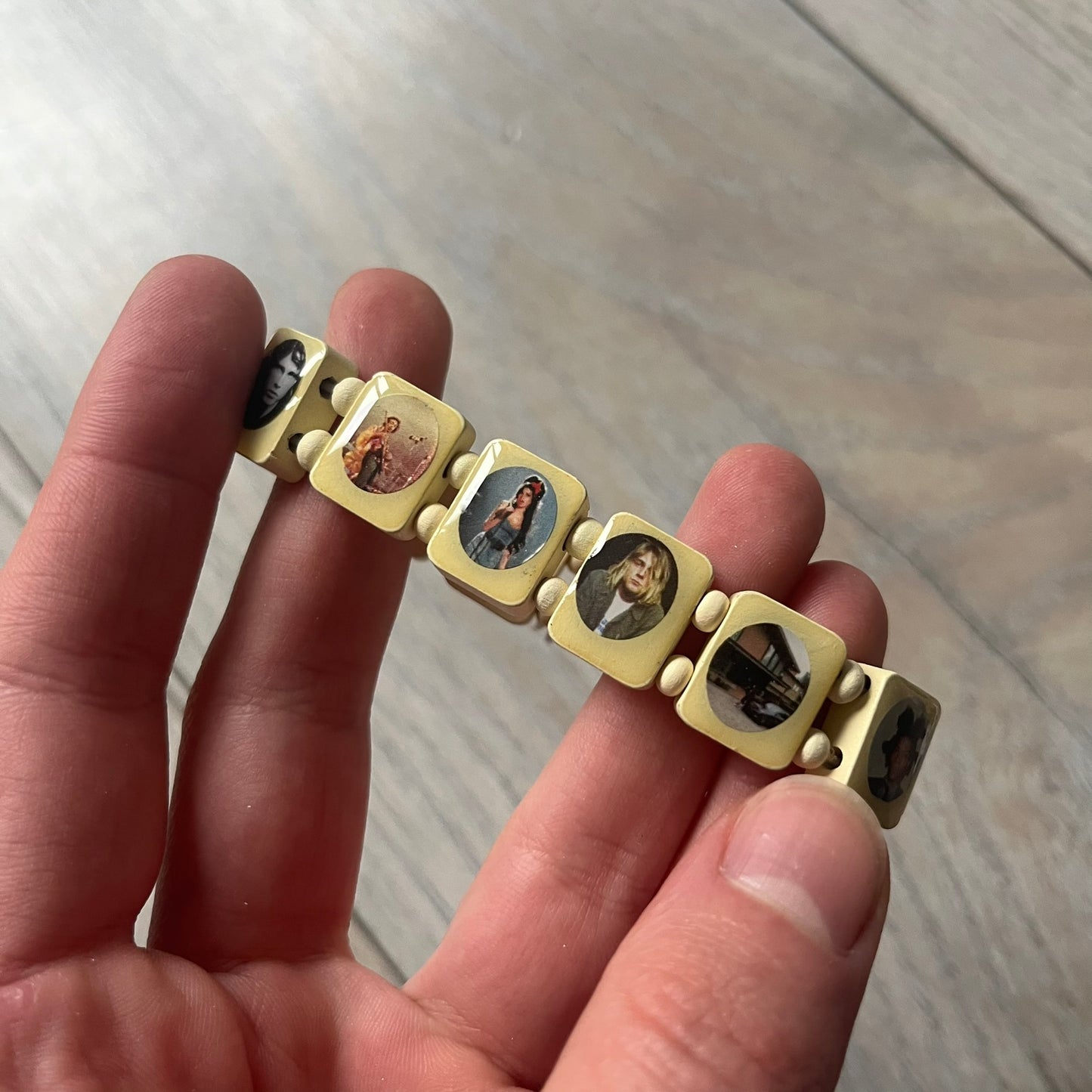 Pastel Yellow “Forever 27 Club” bracelet by Bazo 1199, showcasing painted wooden beads and engraved portraits of legendary artists from the infamous 27 Club like Kurt Cobain, Basquiat, and Fredo Santana. Signed “forever 27 club” and “1199” on the inside.