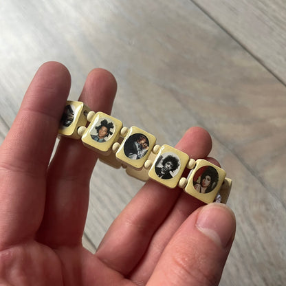 Pastel Yellow “Forever 27 Club” bracelet by Bazo 1199, showcasing painted wooden beads and engraved portraits of legendary artists from the infamous 27 Club like Kurt Cobain, Basquiat, and Fredo Santana. Signed “forever 27 club” and “1199” on the inside.