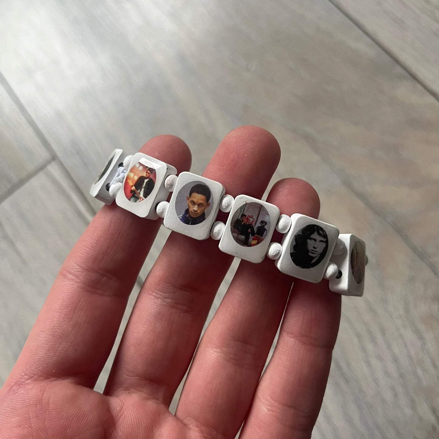 White “Forever 27 Club” bracelet by Bazo 1199, showcasing painted wooden beads and engraved portraits of legendary artists from the infamous 27 Club like Kurt Cobain, Basquiat, and Fredo Santana. Signed “forever 27 club” and “1199” on the inside.