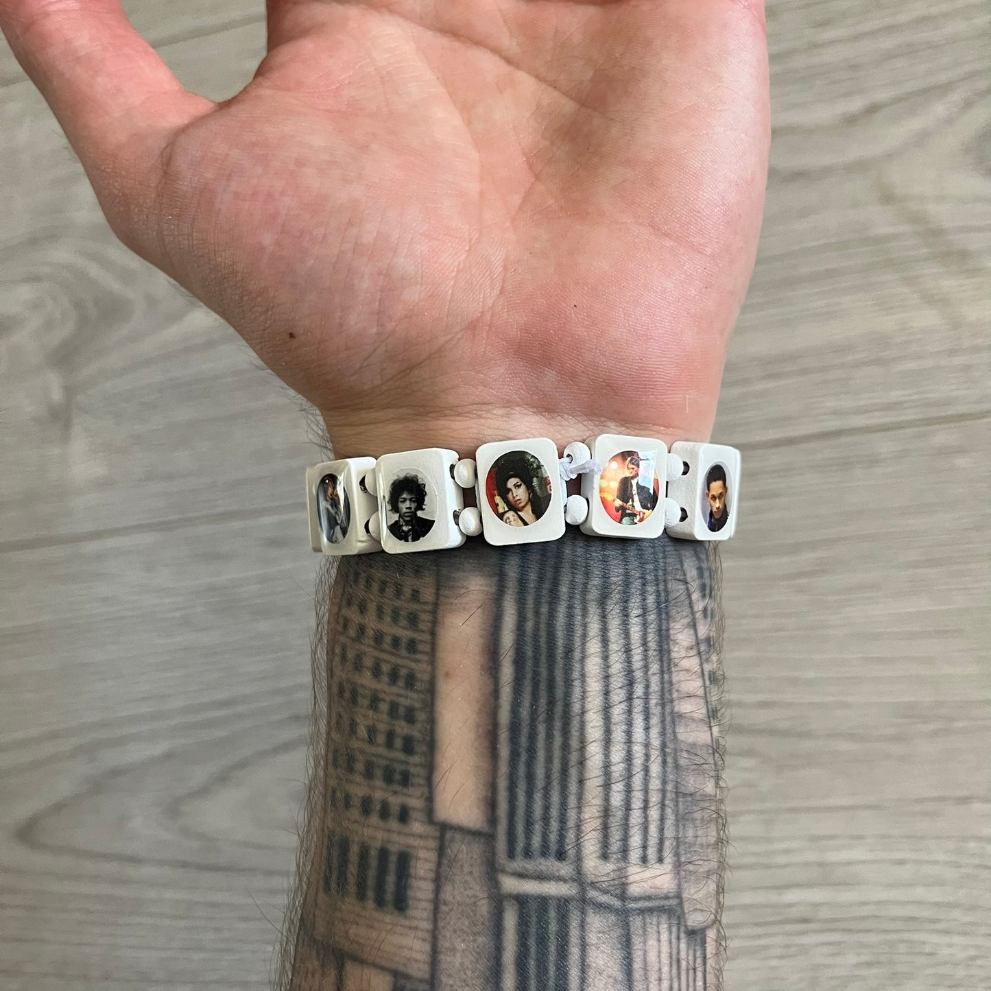 White “Forever 27 Club” bracelet by Bazo 1199, showcasing painted wooden beads and engraved portraits of legendary artists from the infamous 27 Club like Kurt Cobain, Basquiat, and Fredo Santana. Signed “forever 27 club” and “1199” on the inside.