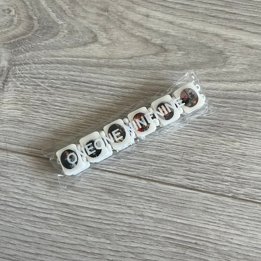 White “Forever 27 Club” bracelet by Bazo 1199, showcasing painted wooden beads and engraved portraits of legendary artists from the infamous 27 Club like Kurt Cobain, Basquiat, and Fredo Santana. Signed “forever 27 club” and “1199” on the inside.