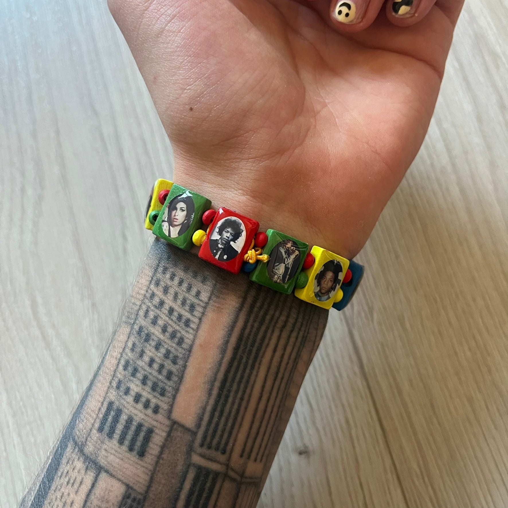 Multicolor “Forever 27” bracelet by Bazo 1199, showcasing painted wooden beads and engraved portraits of legendary artists from the infamous 27 Club like Kurt Cobain, Basquiat, and Fredo Santana. Signed “forever 27” and “1199” on the inside, this piece is a striking nod to music and art history. Limited and highly sought-after, it captures both style and cultural significance.