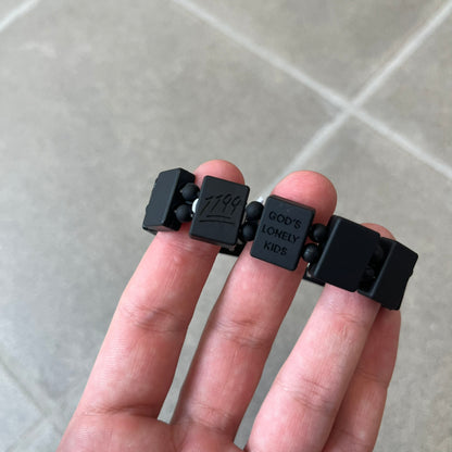 Bazo 1199 “God’s Lonely Kids” Bracelet is a black silicone bead bracelet featuring crystal cross details on the outside of each bead. The interior is engraved with the 1199 logo and “God’s Lonely Kids” text.