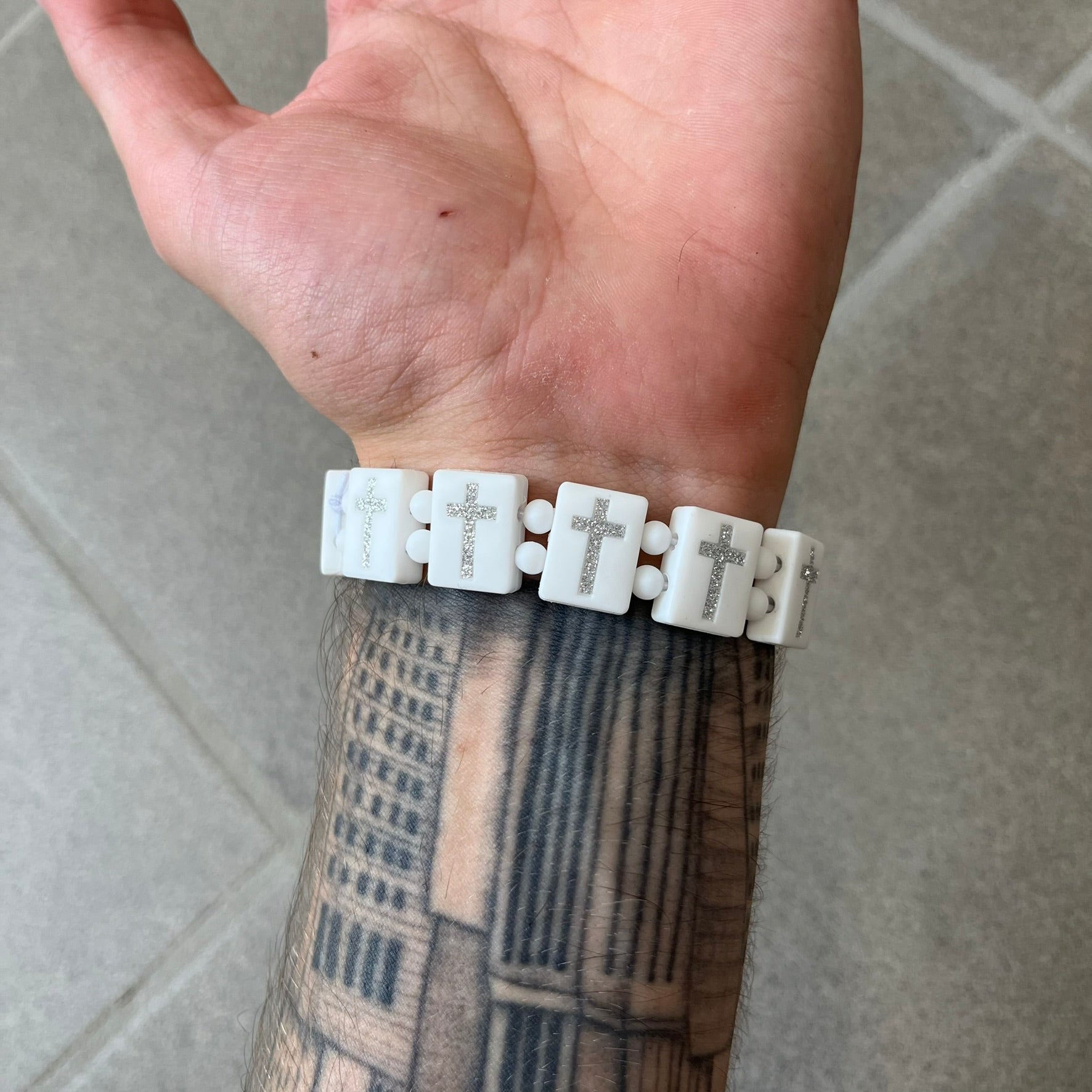 Bazo 1199 “God’s Lonely Kids” Bracelet is a white silicone bead bracelet featuring crystal cross details on the outside of each bead. The interior is engraved with the 1199 logo and “God’s Lonely Kids” text.