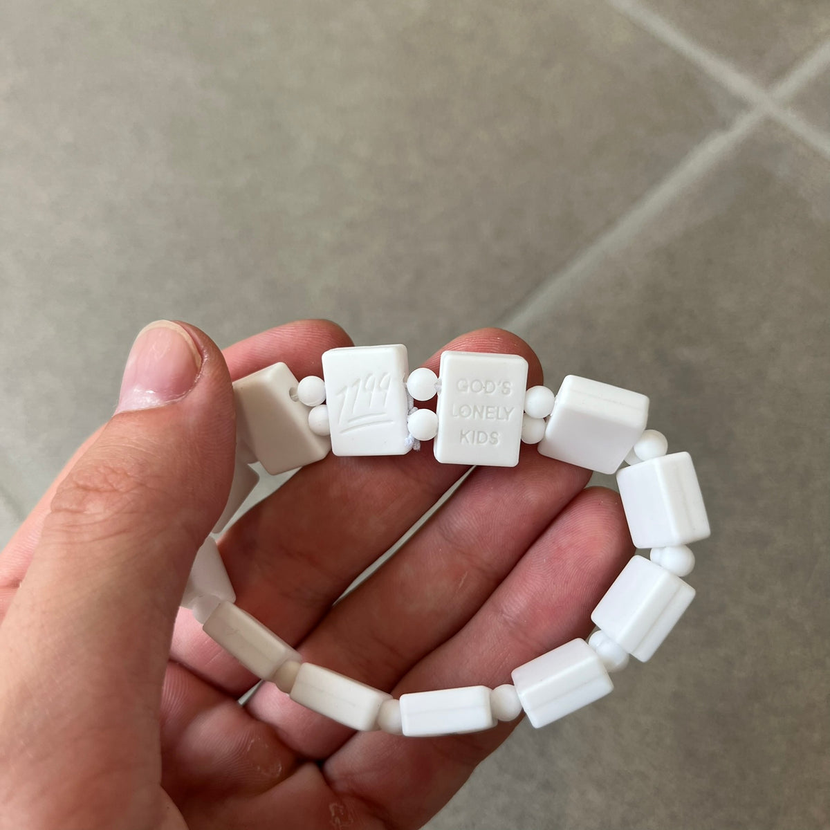 Bazo 1199 “God’s Lonely Kids” Bracelet is a white silicone bead bracelet featuring crystal cross details on the outside of each bead. The interior is engraved with the 1199 logo and “God’s Lonely Kids” text.