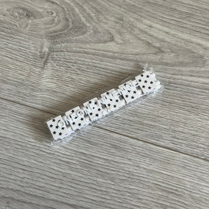Bazo 1199 “White on Black” Stars Bracelet is a acetate bead bracelet featuring white beads with black star graphics printed on the tops and sides. One bead is marked with a red 1199 logo on the inside. It comes with the original foil packaging.
