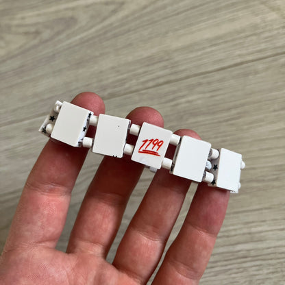 Bazo 1199 “White on Black” Stars Bracelet is a acetate bead bracelet featuring white beads with black star graphics printed on the tops and sides. One bead is marked with a red 1199 logo on the inside. It comes with the original foil packaging.
