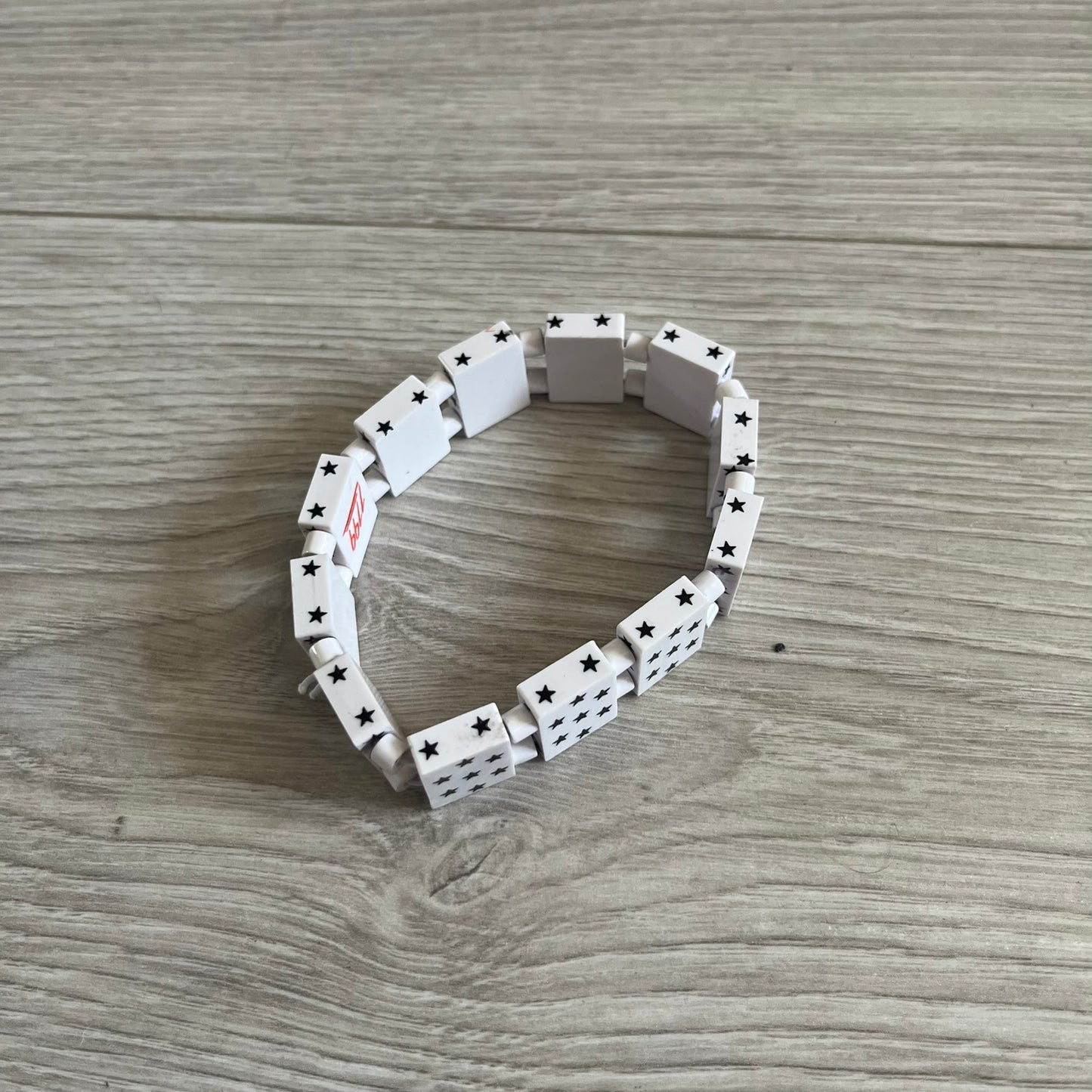 Bazo 1199 “White on Black” Stars Bracelet is a acetate bead bracelet featuring white beads with black star graphics printed on the tops and sides. One bead is marked with a red 1199 logo on the inside. It comes with the original foil packaging.
