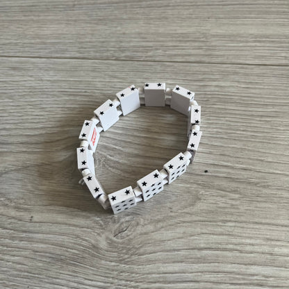 Bazo 1199 “White on Black” Stars Bracelet is a acetate bead bracelet featuring white beads with black star graphics printed on the tops and sides. One bead is marked with a red 1199 logo on the inside. It comes with the original foil packaging.
