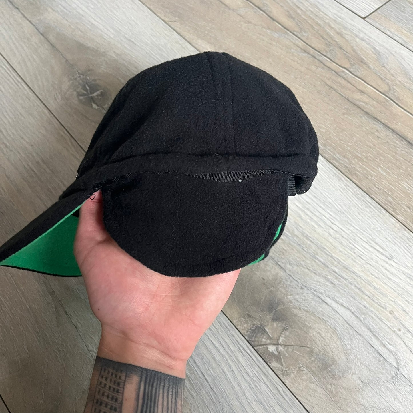 Ben 10 Alien Force Earflap 2011 Hat is a black polyester kids-size hat with green interior lining and earflaps on both sides. The front features embroidered Ben 10 character graphics with “Ben 10 Alien Force” text. Finished with an official 2011 Cartoon Network tag and a soft overall construction.
