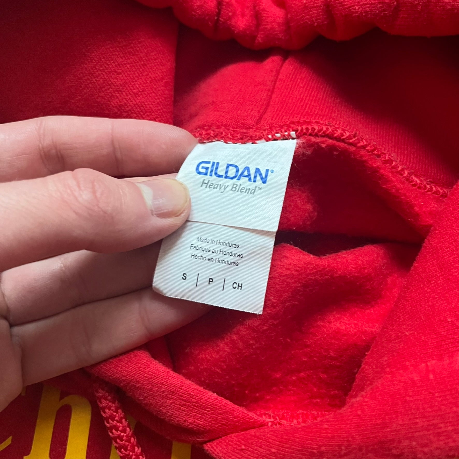 Bevar Christiania Red Hoodie is a red pullover hoodie made on a Gildan Heavy Blend blank, manufactured in Honduras. It features a classic construction with an adjustable hood and a front kangaroo pocket. The front displays yellow “Bevar Christiania” text with three large yellow dots printed underneath.