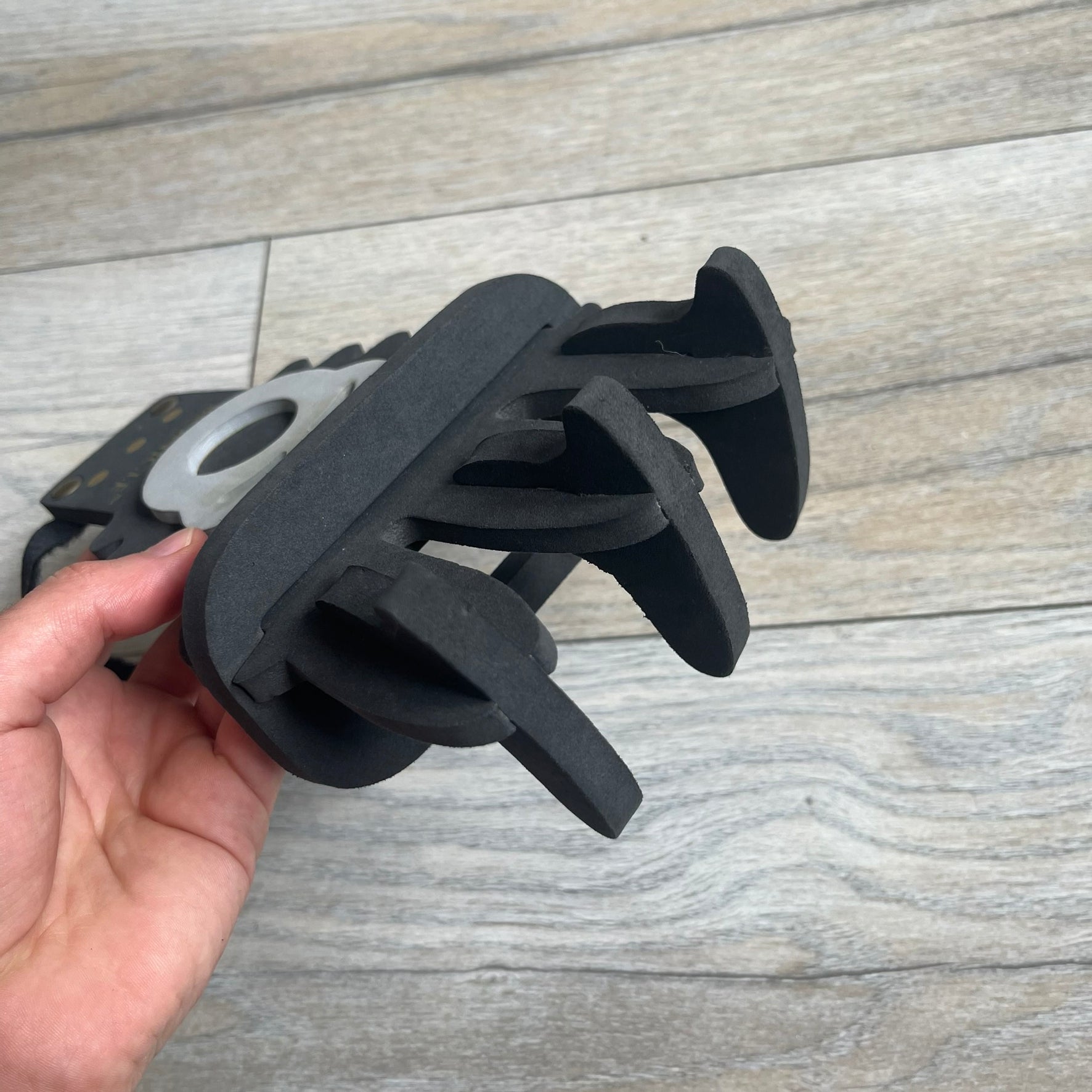 Bionicle 2000s Onua Foam Claw is a black and gray foam weapon featuring three claw tips at the top. It attaches to the wrist with a Velcro strap and is designed to be worn over the hand. The claw is marked with small gray LEGOLAND text and gold Bionicle branding near the bottom.