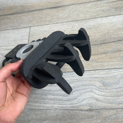 Bionicle 2000s Onua Foam Claw is a black and gray foam weapon featuring three claw tips at the top. It attaches to the wrist with a Velcro strap and is designed to be worn over the hand. The claw is marked with small gray LEGOLAND text and gold Bionicle branding near the bottom.