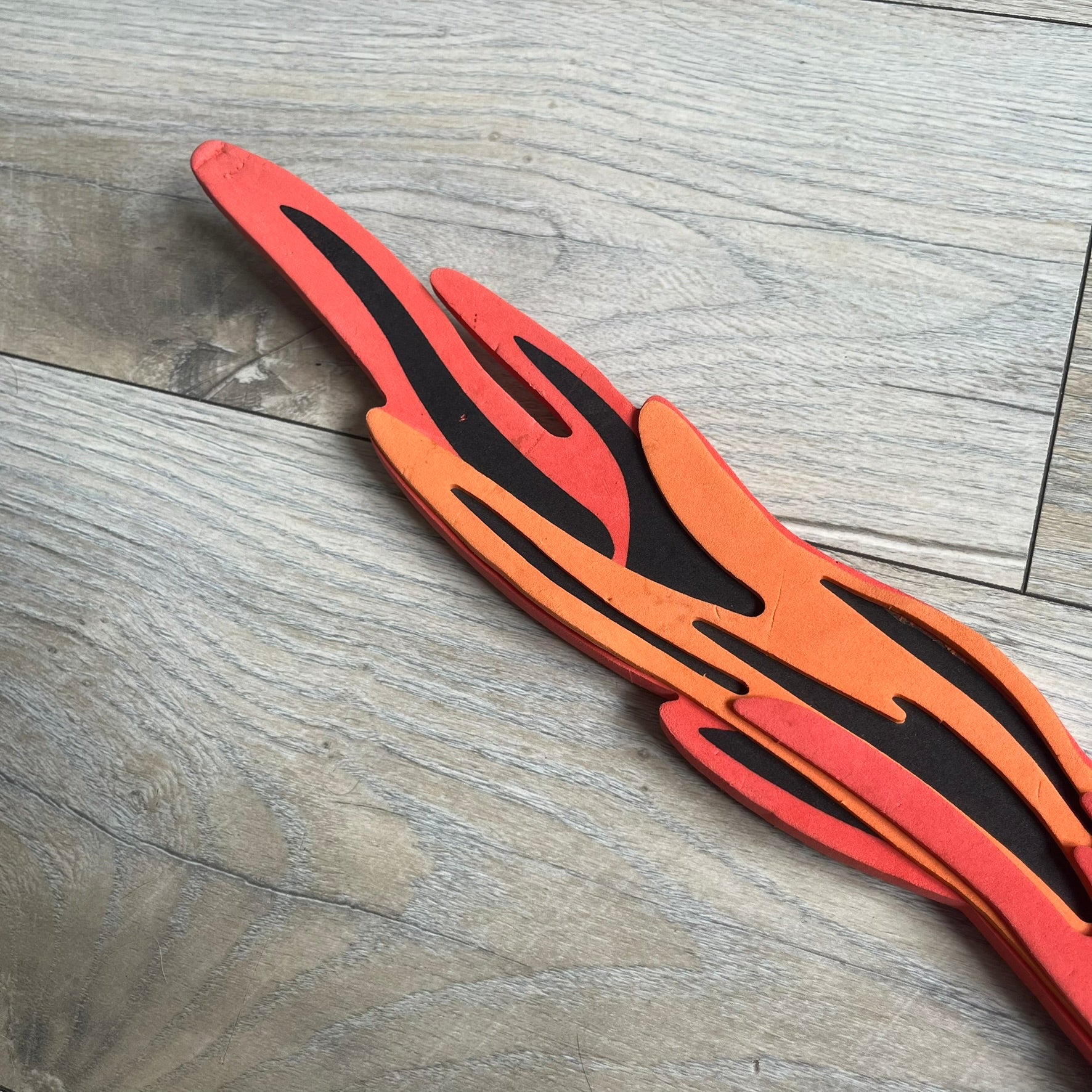 Bionicle 2003 Toa Tahu Flame Sword is a foam toy sword finished in red, orange, and black. The blade features a flame-shaped design at the top, while the handle has a standard grip construction. A small Bionicle mask is attached to the bottom of the handle. The sword is marked with Bionicle and LEGOLAND branding.
