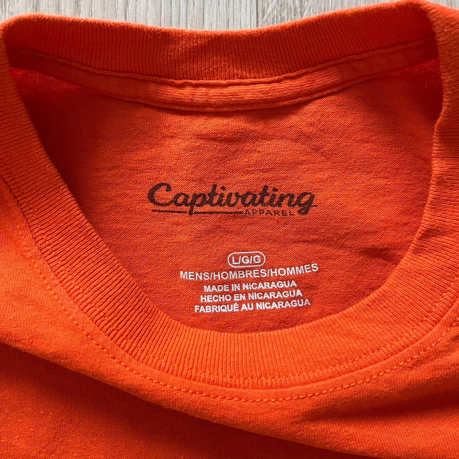 Close-up of an orange shirt with 'Captivating Apparel' branding on the label.