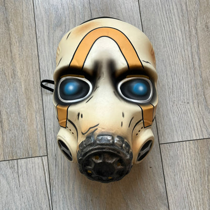 Borderlands 3 Pre-Order Exclusive Psycho Mask is a plastic character mask based on the Psycho enemy from the video game. The mask recreates the character’s white bandit mask design with detailed sculpting and includes an adjustable rubber strap for wearing. The interior features foam padding for a more secure fit on the head. Psychos are one of the most recognizable characters in the Borderlands franchise and appear as masked bandits throughout the series.