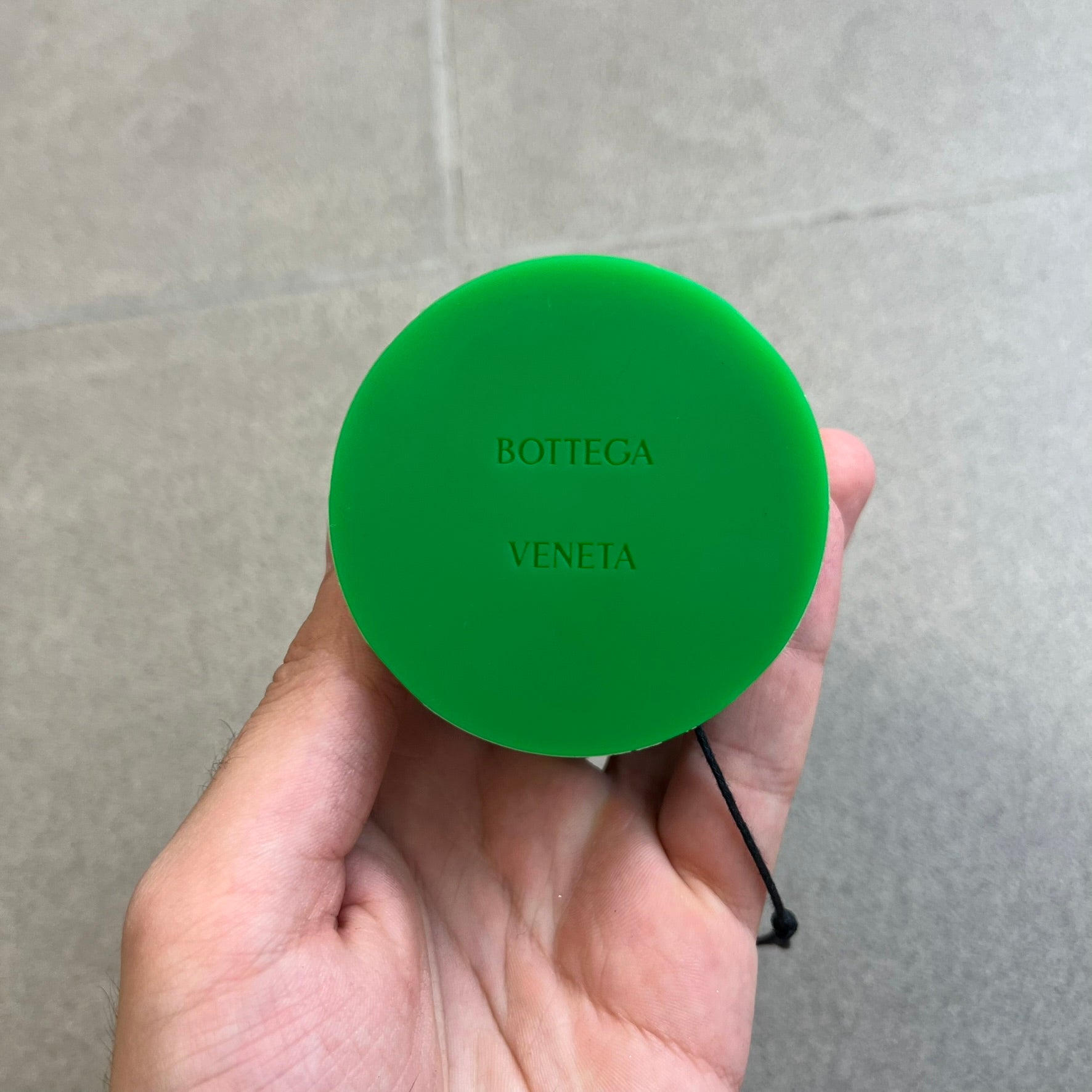 Bottega Veneta Green Rubber Yo-Yo is a collectible accessory crafted from green and black silicone. It features green outer halves with a black center section, a black string, and an engraved Bottega Veneta logo on one side. The yo-yo comes complete with its original box and paper bag.
