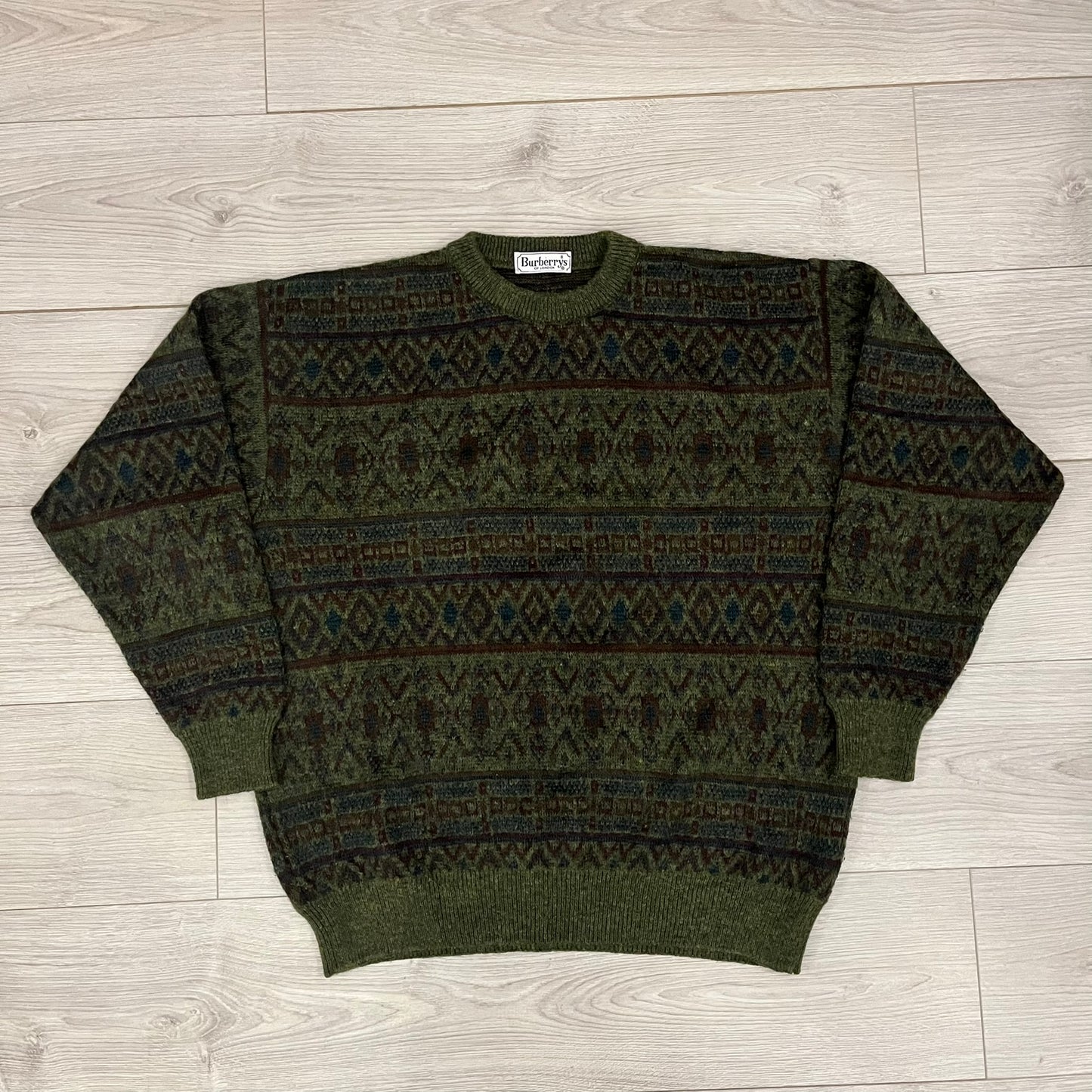 Burberry’s of London 90’s Sweater from 1998/99, crafted from a blend of acrylic, mohair, polyamide, wool, alpaca, and viscose. Features an all-over repeat pattern in green, navy, and brown tones. Vintage piece with original white Burberry tag.