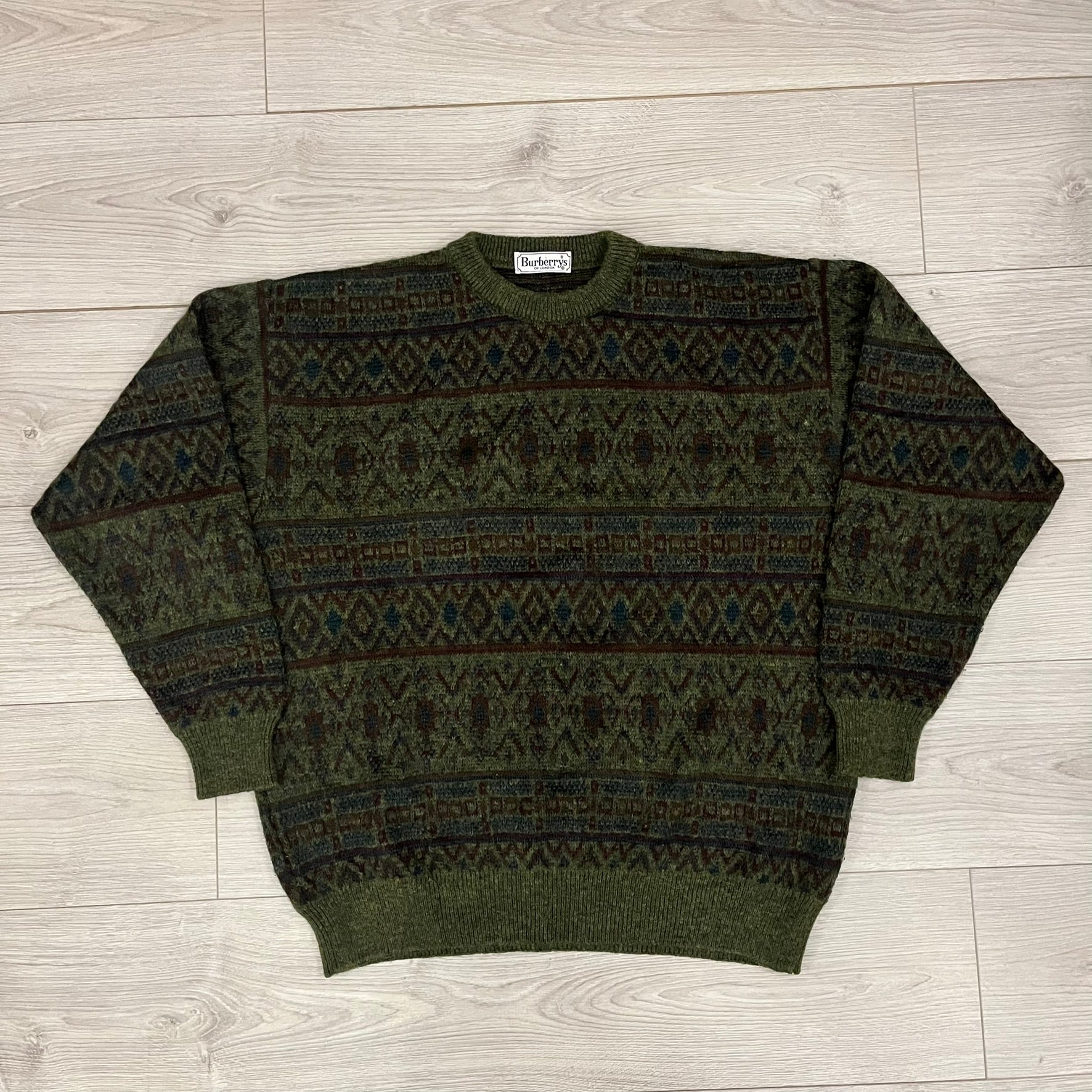Burberry’s of London 90’s Sweater from 1998/99, crafted from a blend of acrylic, mohair, polyamide, wool, alpaca, and viscose. Features an all-over repeat pattern in green, navy, and brown tones. Vintage piece with original white Burberry tag.