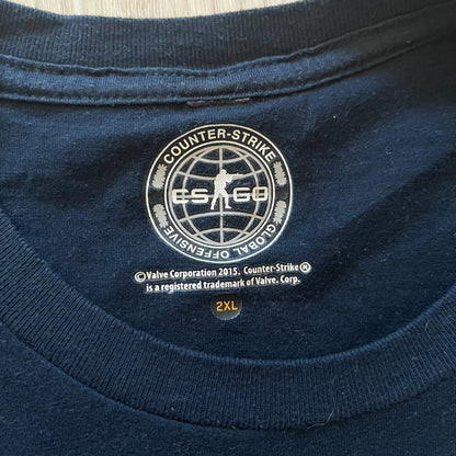 CS:GO 2015 Defuse Kit tee in navy, featuring a bright yellow defuse kit logo on the chest and a small yellow CS:GO patch on the sleeve. Made in Nicaragua from a 60/40 cotton-polyester blend, it includes licensed 2016 Valve Corporation and Counter-Strike Global Offensive tags. A collectible gaming tee that celebrates one of the most iconic in-game items from the series.