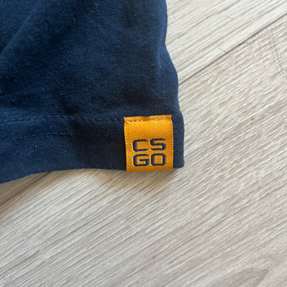 CS:GO 2015 Defuse Kit tee in navy, featuring a bright yellow defuse kit logo on the chest and a small yellow CS:GO patch on the sleeve. Made in Nicaragua from a 60/40 cotton-polyester blend, it includes licensed 2016 Valve Corporation and Counter-Strike Global Offensive tags. A collectible gaming tee that celebrates one of the most iconic in-game items from the series.