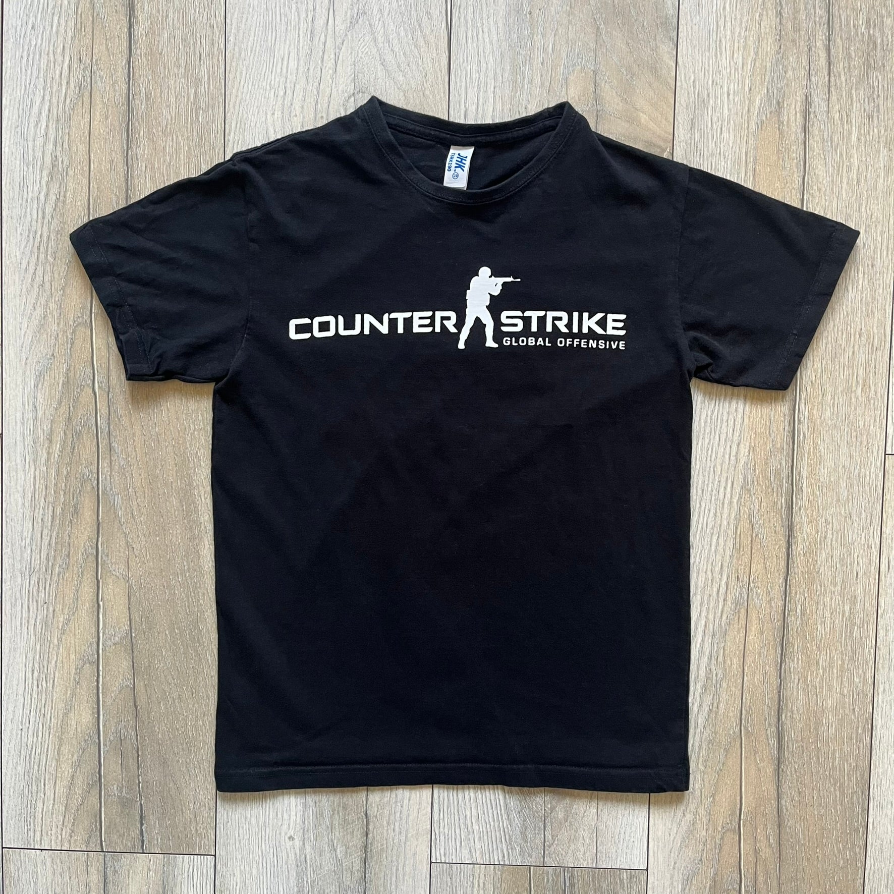 CS:GO Black &amp; White Logo 2010's Tee is a black T-shirt made on a JHK blank. The front features a large white CS:GO logo with an armed figure&nbsp; and “Counter-Strike Global Offensive” text below. Super simple - classic CS logo.